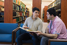 Two male students share book in the college library