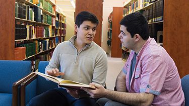 Two male students watching on the book in the library