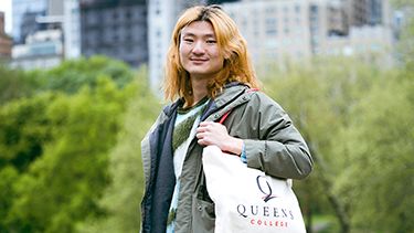 A male student holding Queens college bag and standing outside